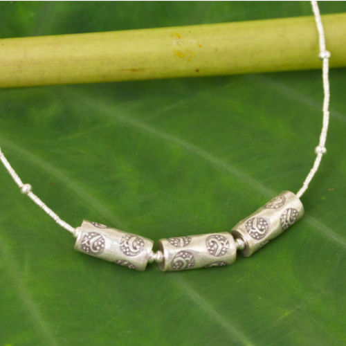 Three 950 silver amulets are engraved with motifs inspired by nature. Centering a necklace of diminutive silver beads, they adorn a necklace by Sasithon Saisuk.